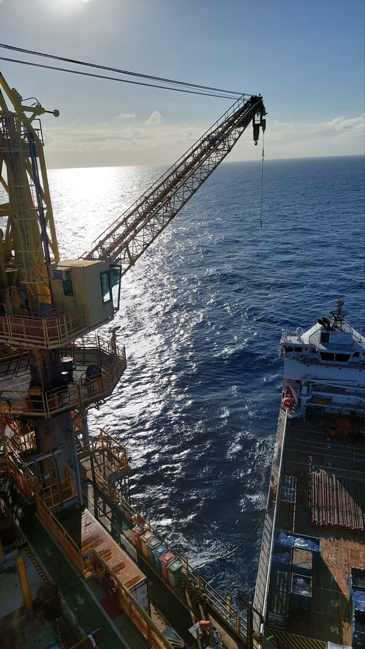 Guindaste da plataforma sobre embarcação de apoio, com o sol no mar