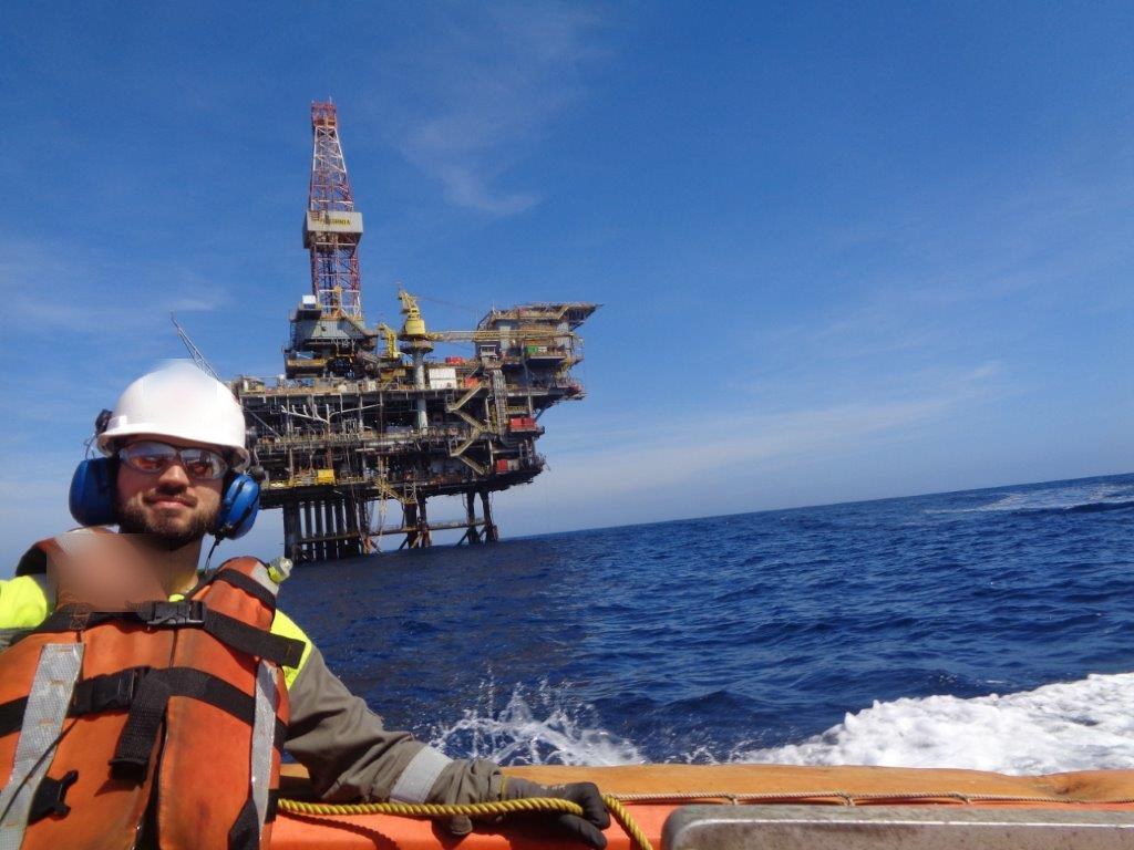 Rafael a bordo do barco de resgate rápido, com capacete, colete e uma plataforma ao fundo