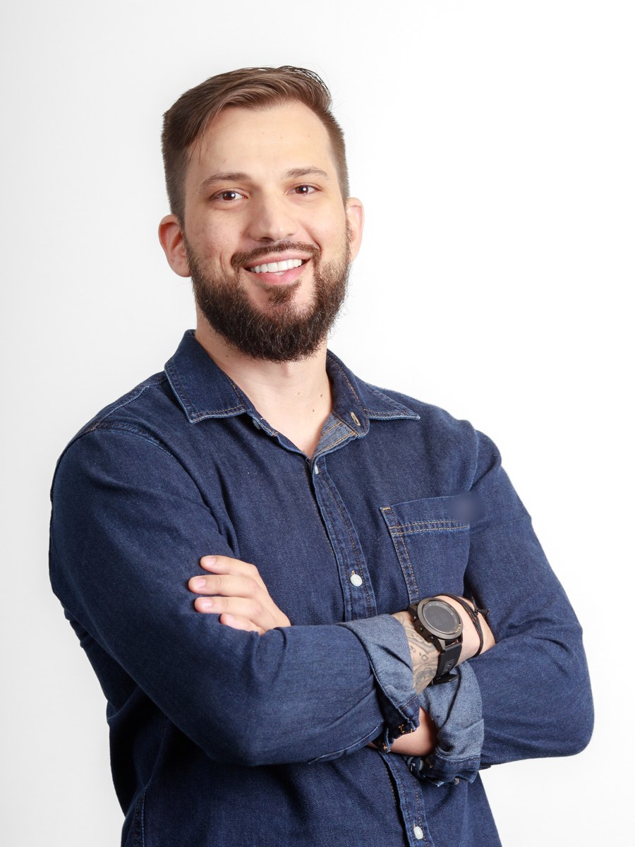 Retrato profissional de Rafael Oertel, de camisa jeans e braços cruzados, sorrindo